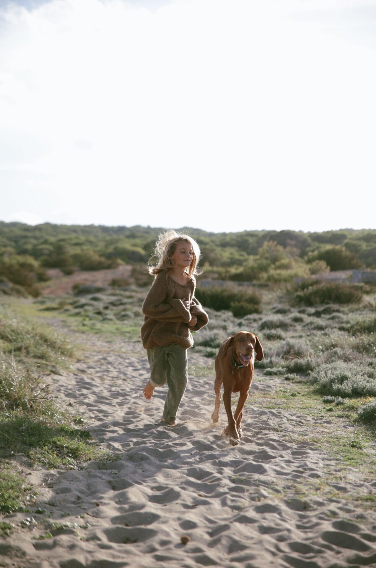 blond model boy long hair summer sunlight running on beach dog
